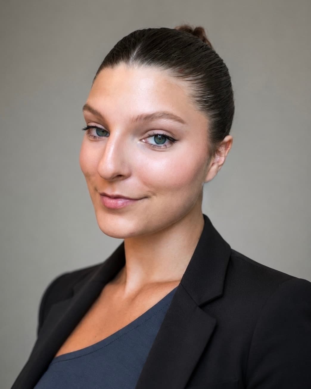 Rylee McGilbery, a professional headshot in a dark blazer against a warm grey backdrop